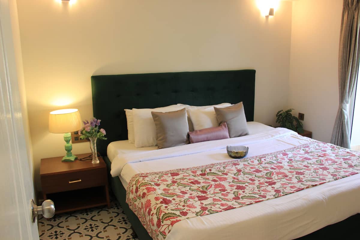 A neatly made bed with a floral bedspread, a green headboard, and a bedside table with a lamp and vase.