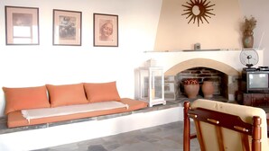 Ein Wohnzimmer mit Kamin aus Stein, einer Couch mit orangefarbenen Kissen und drei gerahmten Bildern an der Wand.