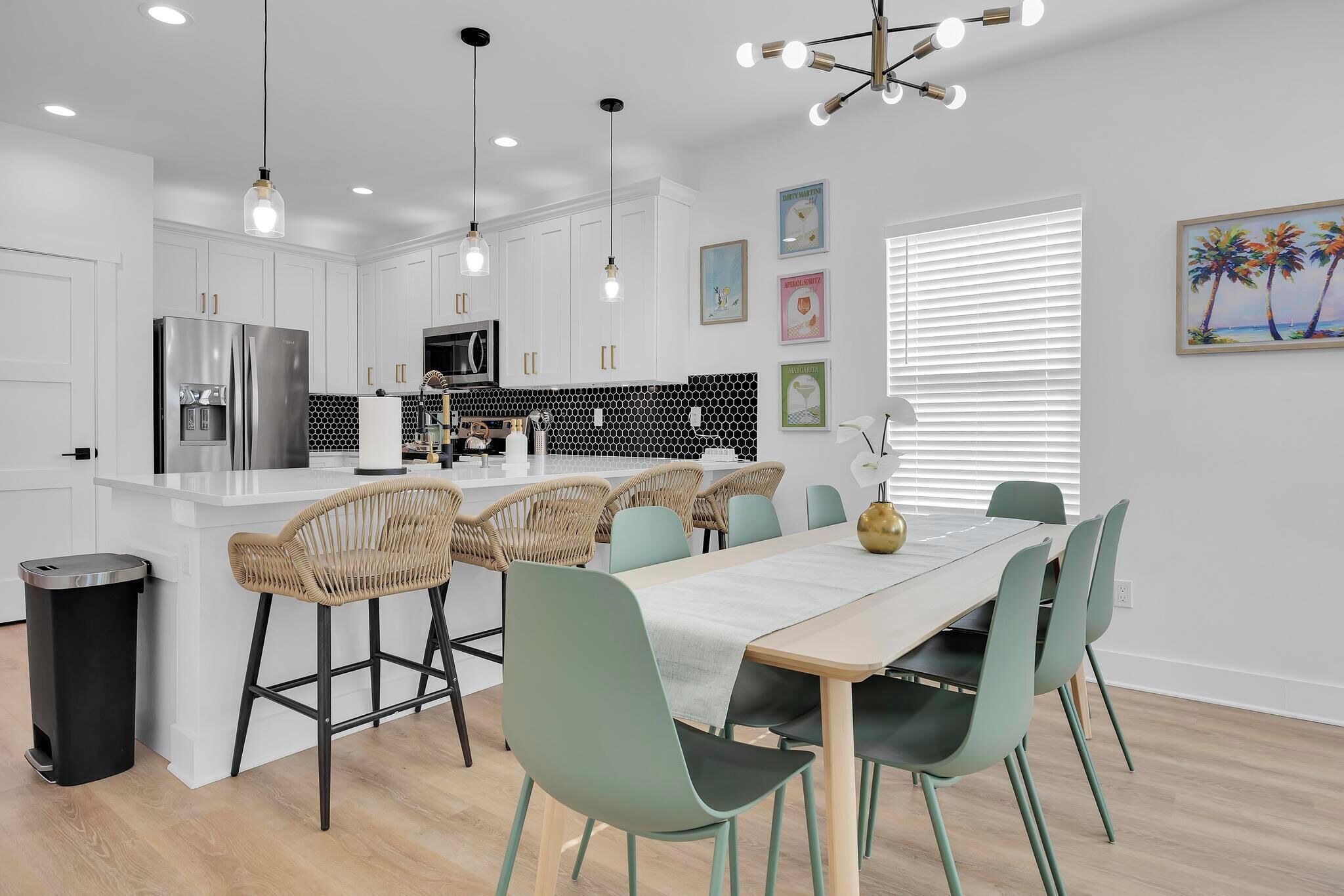 A modern kitchen with white cabinets, a stainless steel refrigerator, and a dining area with a table and chairs.