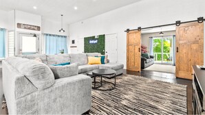 A spacious living room with a grey sectional sofa, a small round table, and a large wooden sliding door leading to an outdoor area.