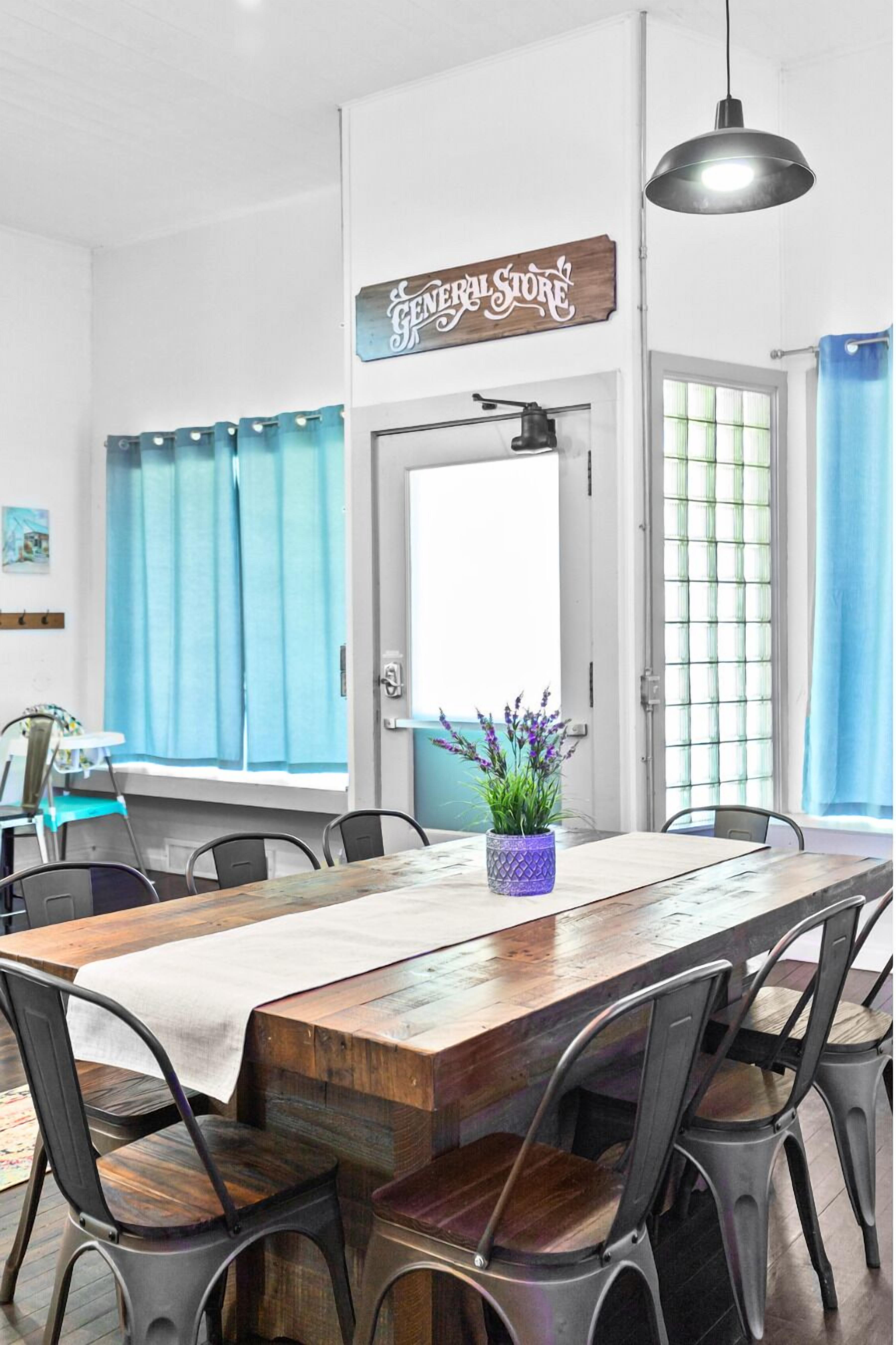 A dining area with a long wooden table, metal chairs, a hanging pendant light, and a sign above the door reading "General Store".