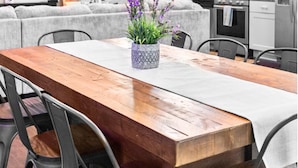 A modern kitchen with a wooden dining table, grey chairs, and a potted plant.