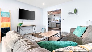 Una sala de estar moderna con televisor de pantalla plana, un sofá, una mesa de centro y vistas a la cocina.
