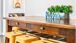 Una cocina con encimera de madera, tres taburetes amarillos, una planta en maceta y un cuadro en la pared.