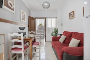 A living room with a red sofa, white chairs, a wooden dining table, and a staircase leading to another room.
