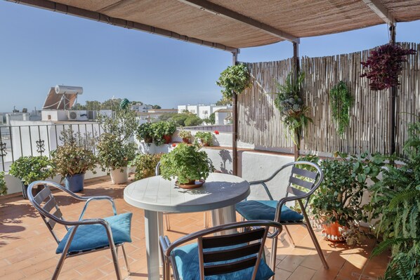 Een terras met een tafel en stoelen, plantenpotten en een uitzicht op gebouwen in de verte.