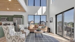 A modern living room with a sofa, coffee table, and large windows offering a view of the outside. - MountainSplash: Pool*MtnView*Pets*Games*HotTub*Wifi*FirePit (Sevierville)