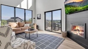 A modern living room with a large window, a fireplace, and a view of the outdoors. - MountainSplash: Pool*MtnView*Pets*Games*HotTub*Wifi*FirePit (Sevierville)