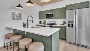 A modern kitchen with a central island, bar stools, a stainless steel refrigerator, and green cabinets. - MountainSplash: Pool*MtnView*Pets*Games*HotTub*Wifi*FirePit (Sevierville)