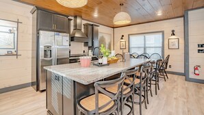 A modern kitchen with a central island, stainless steel appliances, and a dining area with chairs and a table. - MtnPlunge@SC: Pool*MtnViews*Theater*Games*Wifi*HotTub*WaterPark*FirePit (Sevierville)
