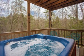 Jacuzzi sobre un pont de fusta amb vista a arbres i muntanyes.