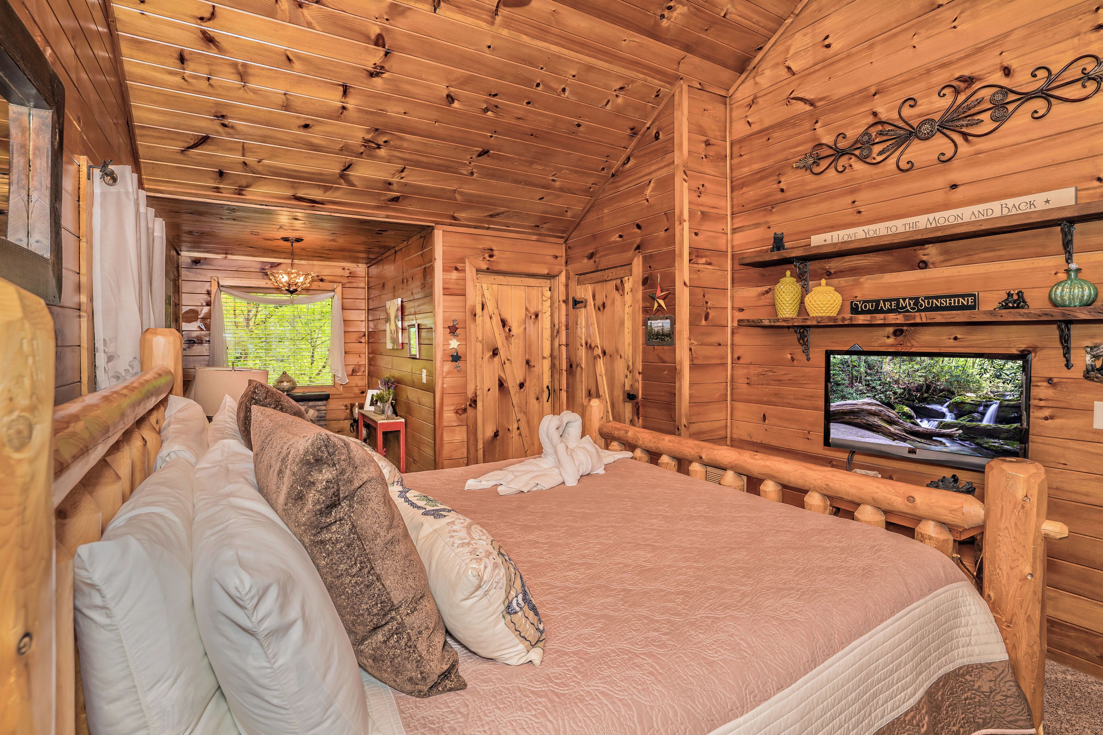 A cozy wooden cabin bedroom with a bed, pillows, a television, and decorative items.