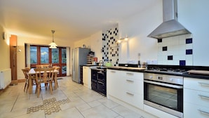 A modern kitchen with a large island, a built-in oven, and a dining area with a wooden table and chairs. - Betws Y Coed Holiday Home by Guestz (Betws-Y-Coed)
