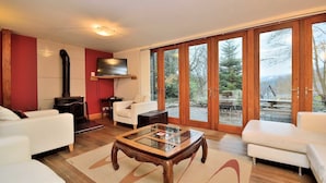 A living room with a fireplace, a television mounted on the wall, and a large sliding glass door leading to an outdoor area. - Betws Y Coed Holiday Home by Guestz (Betws-Y-Coed)