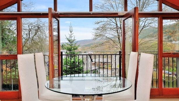 A balcony with a glass table and chairs, offering a view of a mountainous landscape. - Betws Y Coed Holiday Home by Guestz (Betws-Y-Coed)