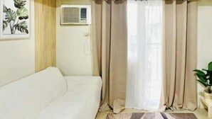 A room with a white sofa, a patterned rug, beige curtains, and an air conditioning unit on the wall. - Cozy Staycation at Avida Iloilo (Iloilo)