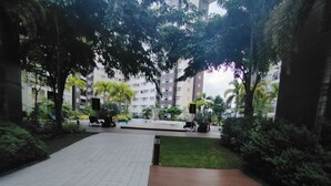 A paved walkway with a tiled area and a wooden deck, surrounded by greenery and a building in the background. - Cozy Staycation at Avida Iloilo (Iloilo)