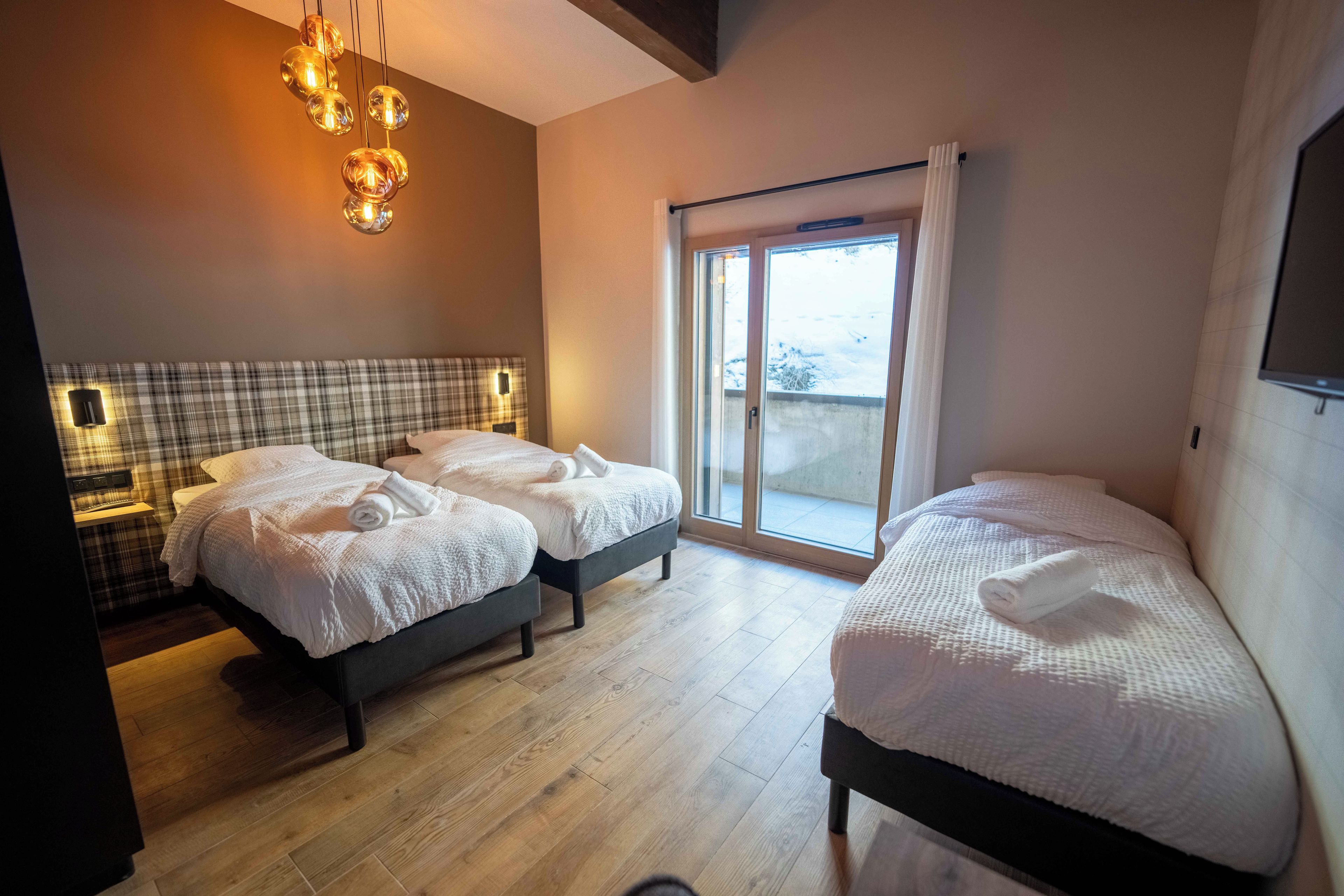 A hotel room with two beds, a large window, and a modern chandelier.