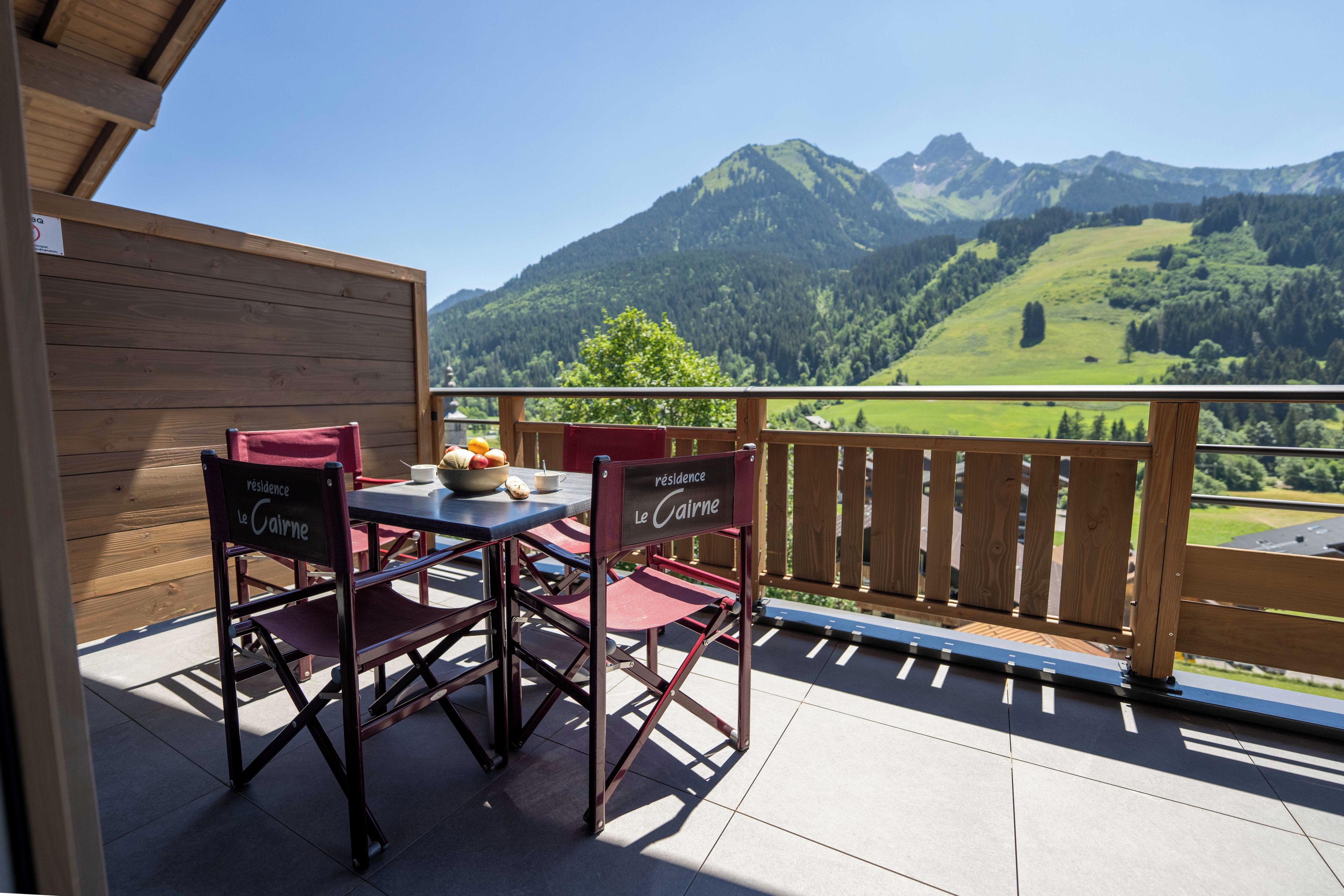 A wooden deck with a table and chairs, overlooking a mountainous landscape.