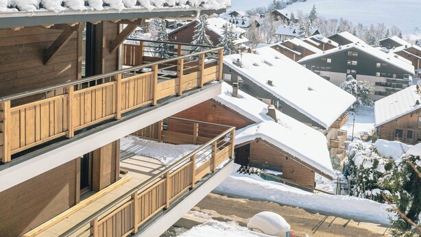 Un edificio de madera de varios pisos con balcones, rodeado de montañas y árboles cubiertos de nieve.