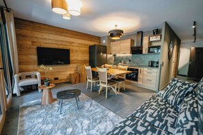 Una cocina moderna con armarios de madera, un comedor con mesa y sillas, un televisor integrado y un sofá en la sala.