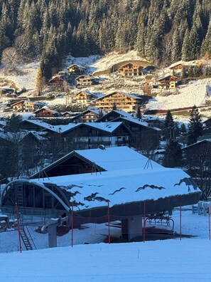 Un pueblo cubierto de nieve con edificios de madera tradicionales, un telesilla y un paisaje montañoso.