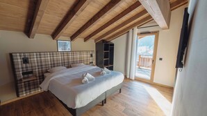 Un dormitorio con cama, vigas de madera, cabecera a cuadros, un estante pequeño y vistas al exterior.