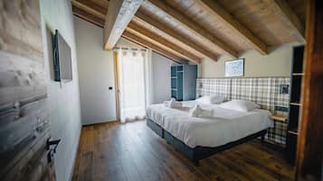 Une chambre avec un plafond en bois, un lit avec une literie blanche, une tête de lit à carreaux et une fenêtre ornée de rideaux légers.