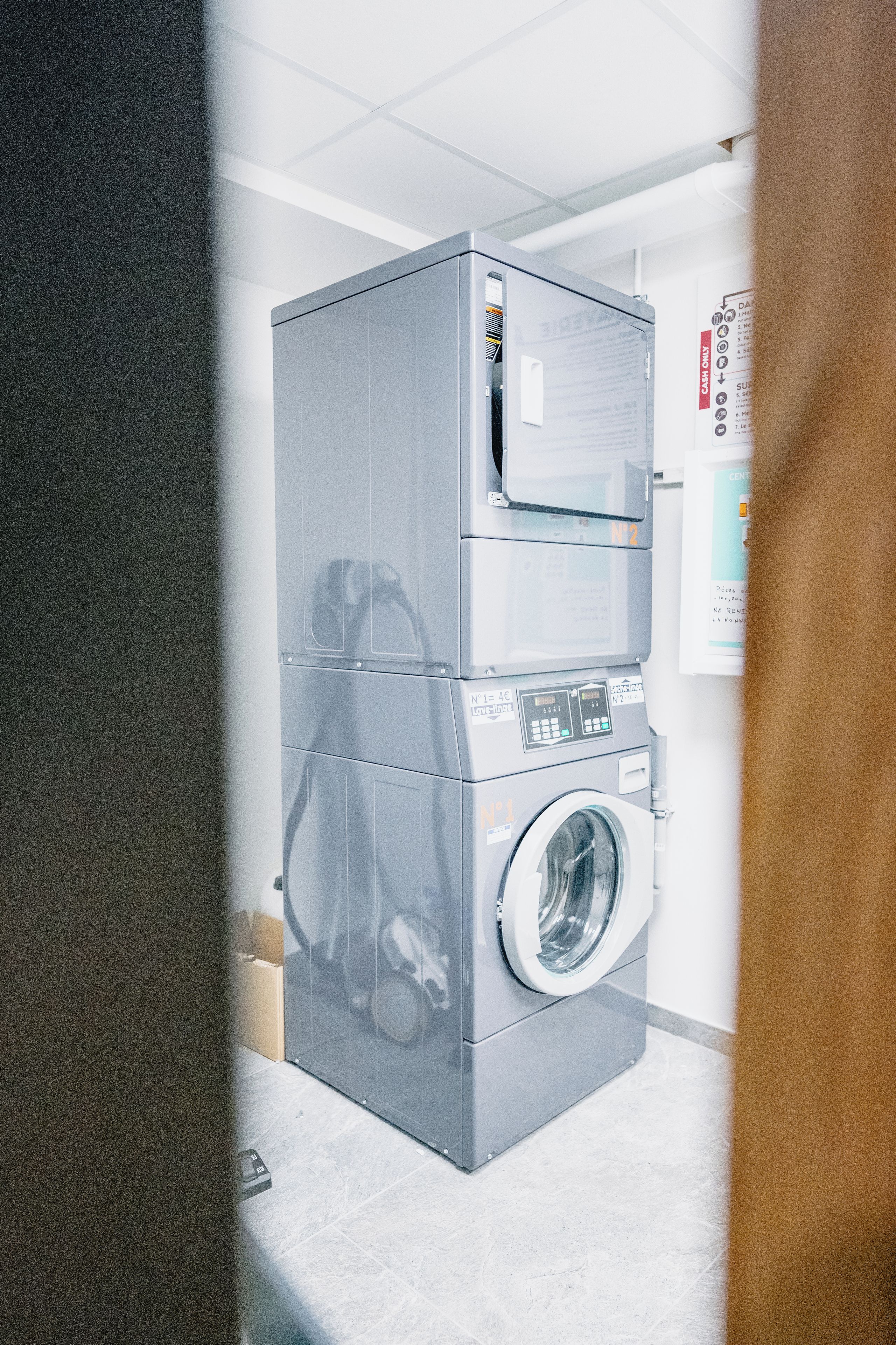 Une machine à laver et un sèche-linge superposés dans une pièce dont le sol est carrelé et le plafond est blanc.