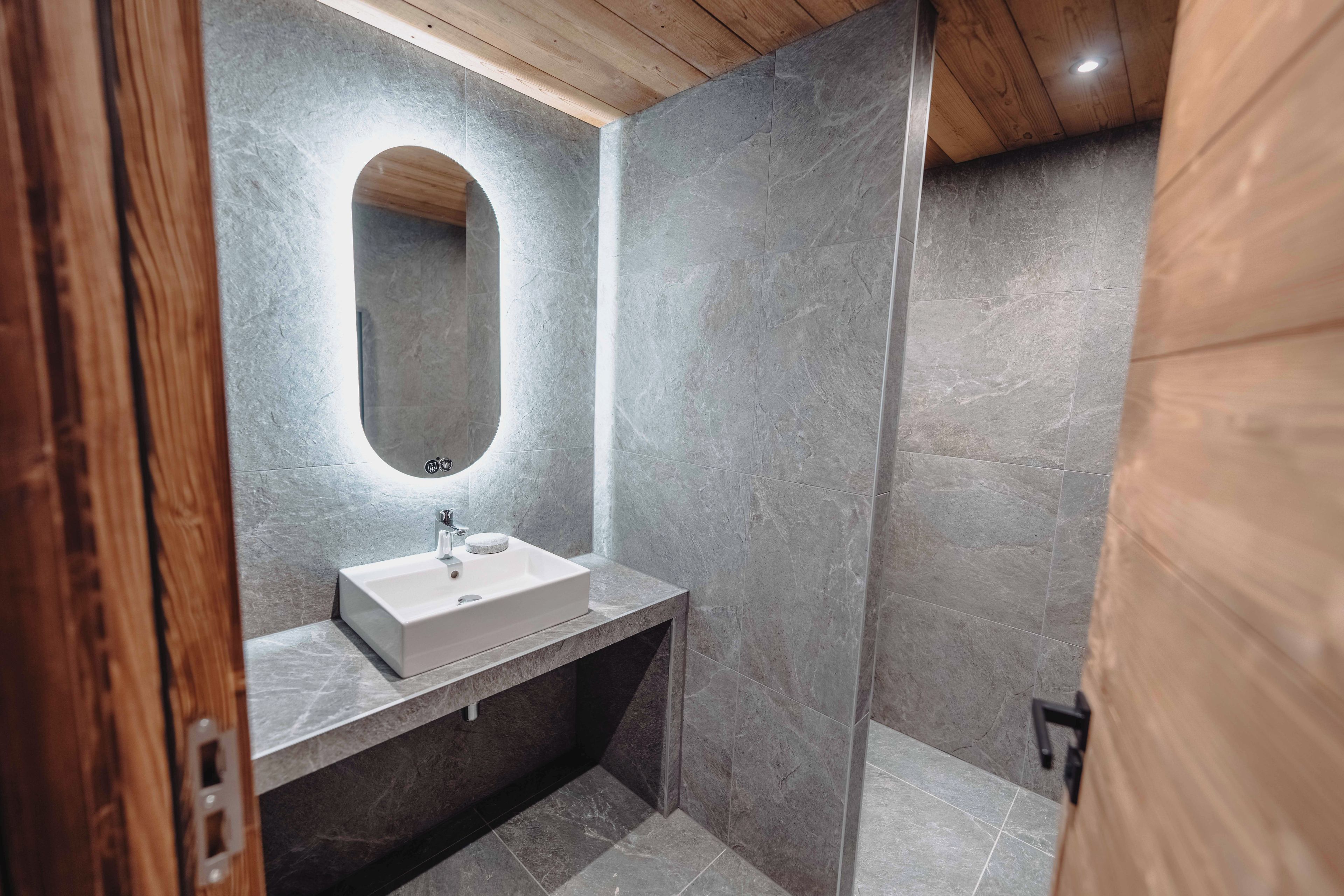 Une salle de bain moderne avec un lavabo blanc, un miroir et un espace douche.