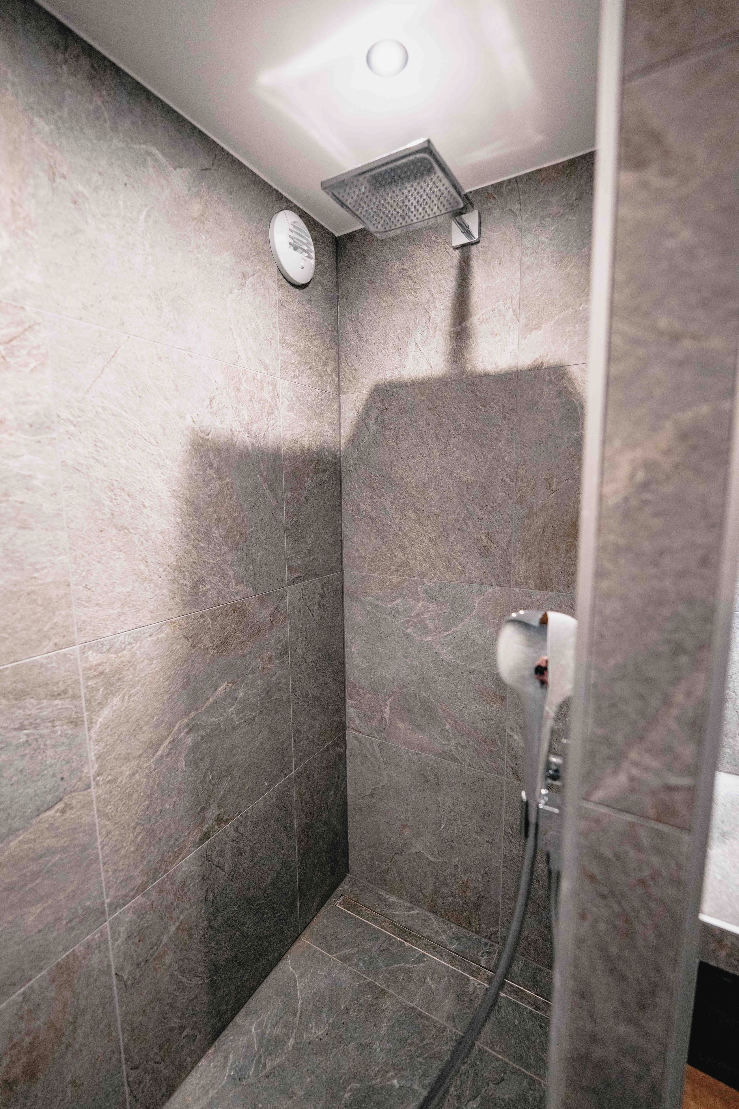 A shower area with a handheld showerhead and a wall-mounted control panel.