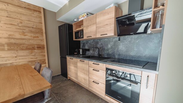 A modern kitchen with wooden cabinets, a black countertop, a built-in oven, and a microwave. - Le Cairne Residence (La Chapelle-d'Abondance)