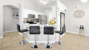 Een moderne keuken met witte kasten, een centraal eiland met barstoelen en een decoratieve gouden vaas.