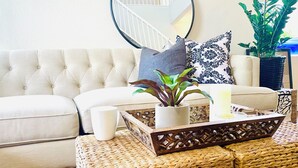 Een woonkamer met een gestoffeerde bank, een bijzettafeltje met een plant, een witte mok en een decoratief dienblad.