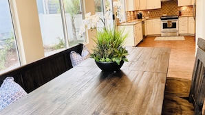 Een moderne keuken met witte kasten, een houten eettafel en een plant in pot.