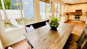 Een moderne keuken met witte kasten, een houten eettafel en een groot raam met uitzicht op een tuin.