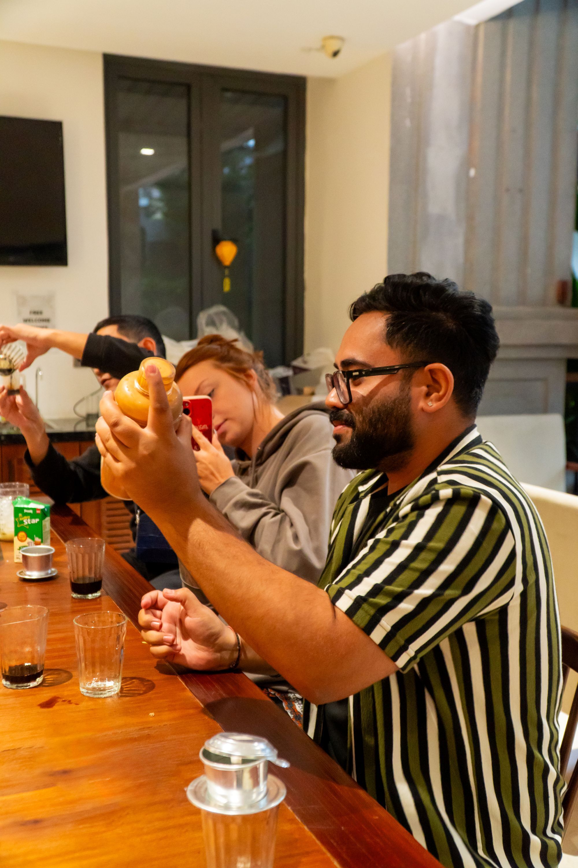 A dining area with a wooden table, glasses, and a person holding a bottle.