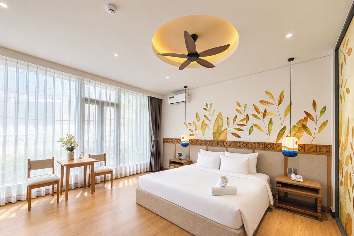 Habitación de hotel con una cama grande, un escritorio con silla, un ventilador de techo y una pared con diseños de hojas.