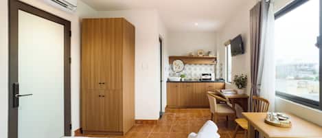 A hotel room with a bed, a desk, a chair, a small kitchenette, and a window with a city view.