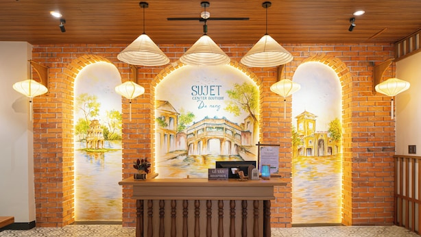 A reception area with a brick wall, a reception desk, and three hanging lamps. - Sujet Center Hotel by Haviland  (Da Nang)