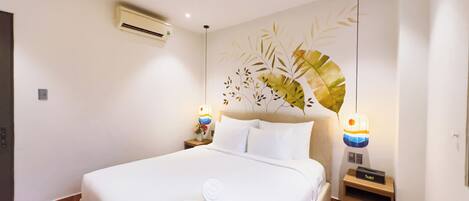 Habitación de hotel con cama, ventilador de techo, aire acondicionado de pared, un adorno en la pared y lámparas de noche.