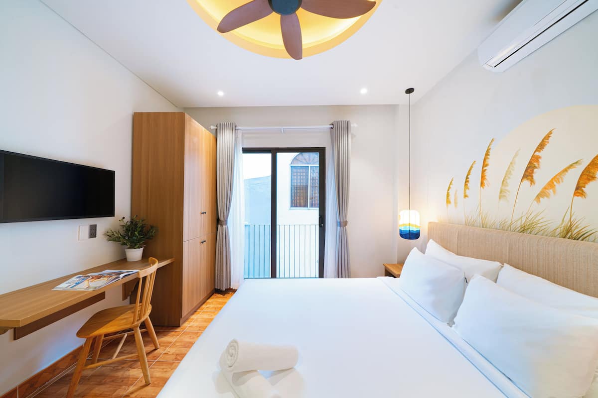 Habitación de hotel con cama, escritorio, silla, televisor, ventilador de techo y vistas al exterior.
