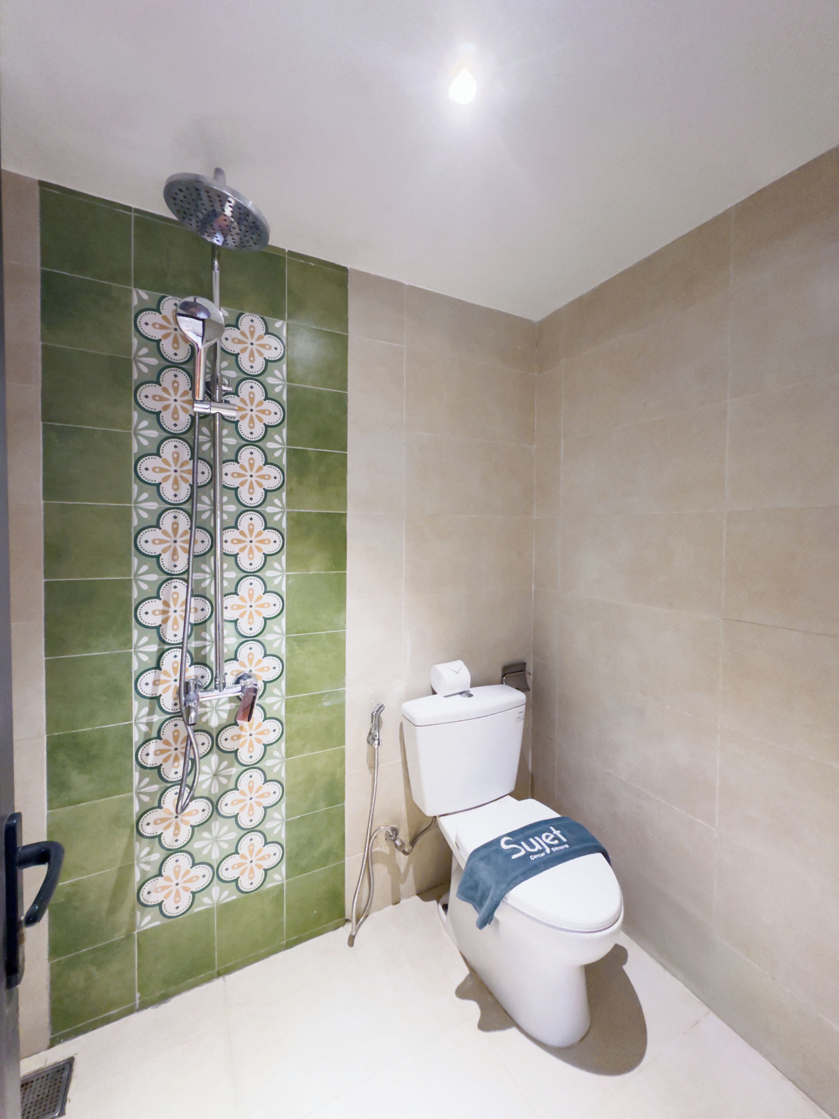 Un baño con ducha, inodoro y baldosas de color verde con diseño.