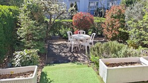 A patio with a table and chairs, surrounded by various plants and a small lawn area.