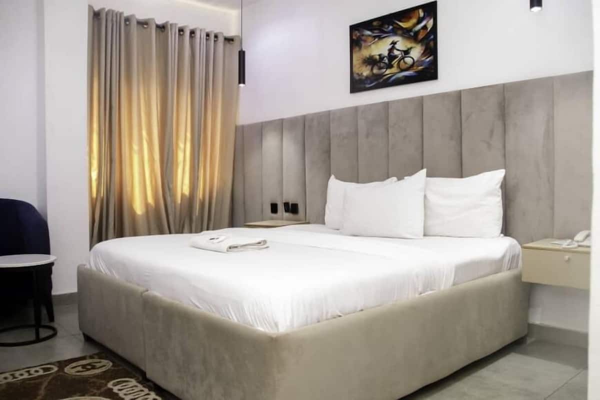 A hotel room with a large bed, a bedside table, a chair, and a painting on the wall.