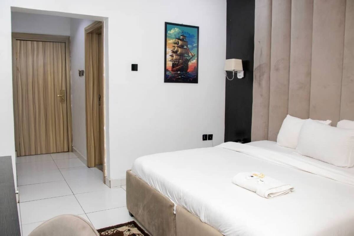 A hotel room with a large bed, a painting on the wall, and a door leading to another room.