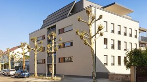 Een modern gebouw met een plat dak, veel ramen en een parkeerplaats met auto's.