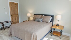 A bedroom with a bed, two bedside tables, a wooden door, and a small table with a lamp. - Mabel's Place - 3BR, 2.5BA, Newly Renovated Duplex (Waynesville)
