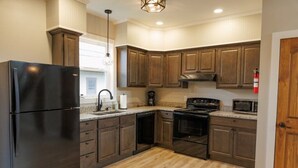 A modern kitchen with dark wooden cabinets, a black refrigerator, a microwave, and a stove. - Mabel's Place - 3BR, 2.5BA, Newly Renovated Duplex (Waynesville)