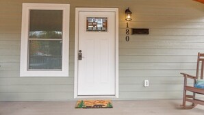 A house with a white door, a window with blinds, a porch with a rocking chair, and a mailbox with the number 180. - Mabel's Place - 3BR, 2.5BA, Newly Renovated Duplex (Waynesville)
